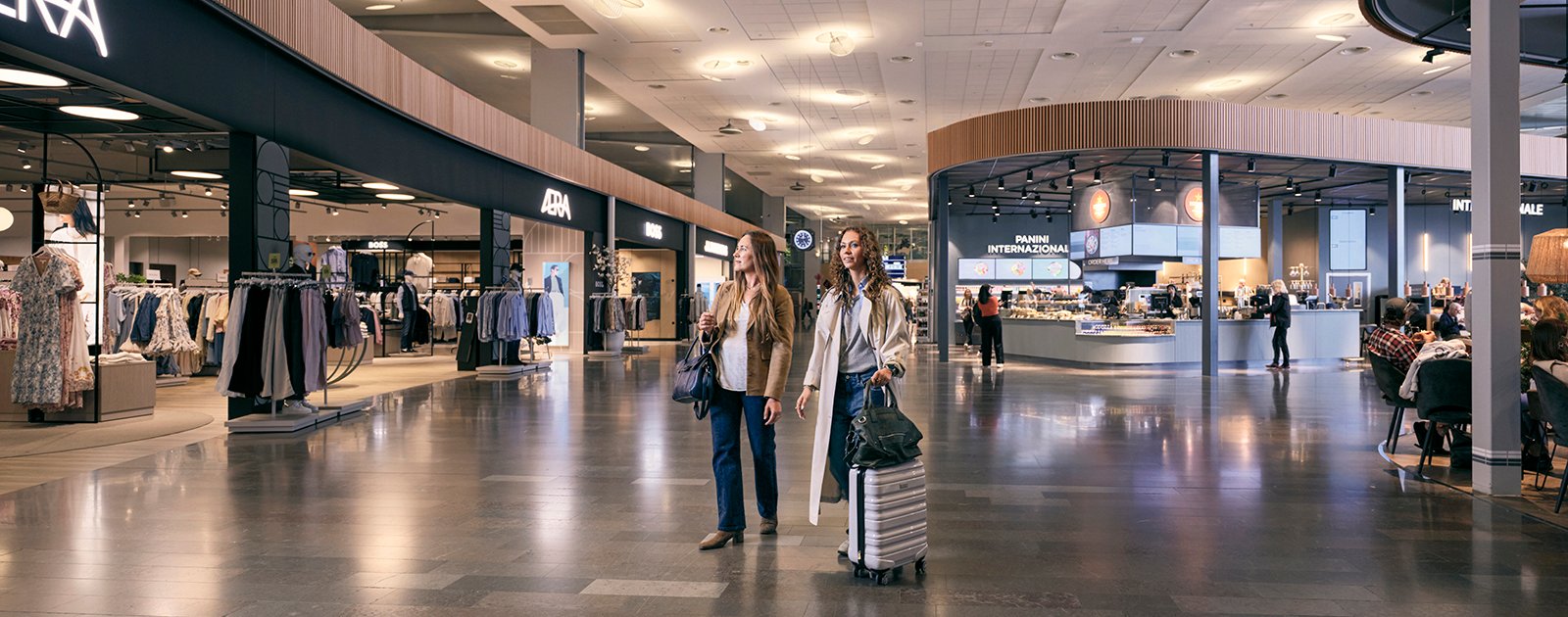 Två kvinnor med resväskor som shoppar på Marknadsplatsen, Arlanda, innan avgång.